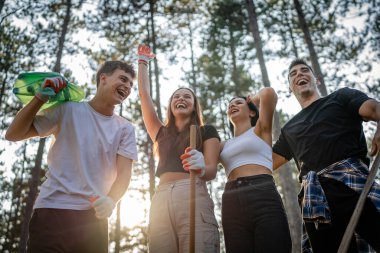 Bir grup genç arkadaş Z erkek ve beyaz kadın atık plastik şişeleri ve kağıtları toplayarak güneşli bir günde çevre koruma kavramının doğasını temizliyorlar.