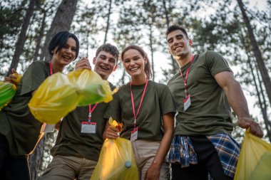 Bir grup genç arkadaş Z erkek ve beyaz kadın atık plastik şişeleri ve kağıtları toplayarak güneşli bir günde çevre koruma kavramının doğasını temizliyorlar.