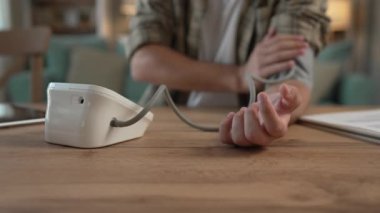 Kafkasyalı genç bir adam masada oturuyor. Kan basıncını ölçmek için evde gerçek sağlık hizmetleri konseptini kullanıyor.