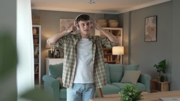 自宅で10代の少年スタンドの肖像画 家庭で音楽を再生するためのヘッドフォン回答スマートフォン — ストック動画