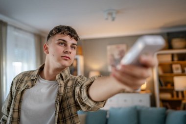 Genç beyaz adam televizyon veya klima için uzaktan kumanda kullanıyor.