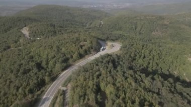 Sırbistan 'da yeşil ve manzara taşımacılığı ve seyahat konseptiyle çevrili dolambaçlı yol boyunca giden bahar aracı kamyonları sırasında bir dağ sırasındaki eğri asfalt bir yolun hava aracı görüntüleri