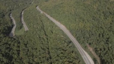 Sırbistan 'da yeşil ve manzara taşımacılığı ve seyahat konseptiyle çevrili dolambaçlı yol boyunca giden bahar aracı otomobili sırasında, bir dağ sırasındaki eğimli asfalt bir yolun hava aracı görüntüleri