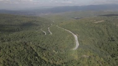 Sırbistan 'da yeşil ve manzara taşımacılığı ve seyahat konseptiyle çevrili dolambaçlı yol boyunca giden bahar aracı otomobili sırasında, bir dağ sırasındaki eğimli asfalt bir yolun hava aracı görüntüleri