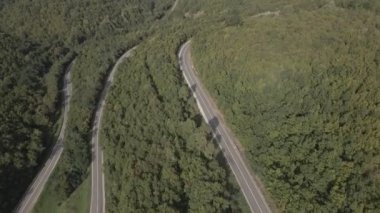 Sırbistan 'da yeşil ve manzara taşımacılığı ve seyahat konseptiyle çevrili dolambaçlı yol boyunca giden bahar aracı otomobili sırasında, bir dağ sırasındaki eğimli asfalt bir yolun hava aracı görüntüleri