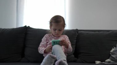 Bir kız çocuğu cep telefonuyla video oyunu oynuyor.