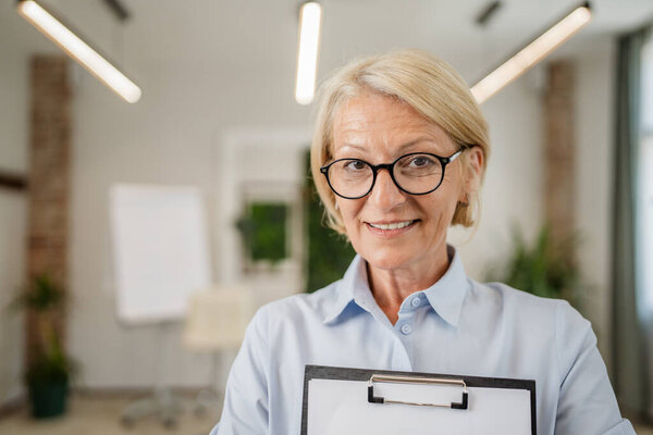 Portrait of one mature blonde caucasian woman with eyeglasses in the office at work happy smile looking to the camera confident copy space