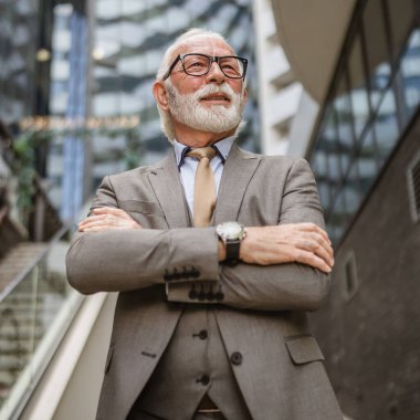 Takım elbiseli kıdemli işadamının portresi modern inşaat şirketinin önünde duruyor.