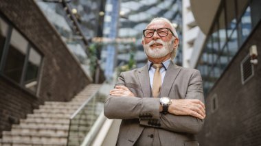 Takım elbiseli kıdemli işadamının portresi modern inşaat şirketinin önünde duruyor.