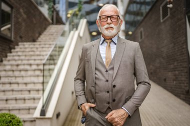 Takım elbiseli kıdemli işadamının portresi modern inşaat şirketinin önünde duruyor.