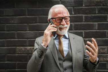 Takım elbiseli kıdemli bir işadamının portresi modern inşaat şirketinin önünde duruyor cep telefonu akıllı telefonu kullanıyor gerçek insan konuşmaları yapıyor.