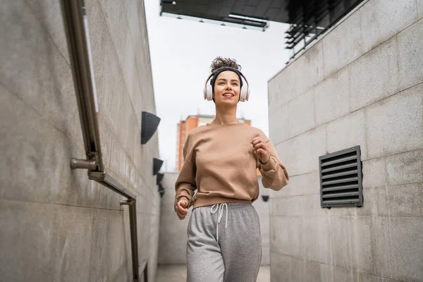 One woman young adult generation z caucasian modern female with headphones and happy smile training in the city run jogging running on the steps real person copy space
