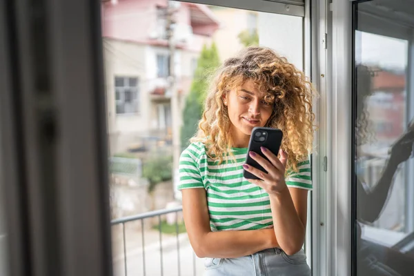 Yetişkin Bir Beyaz Kadın Yatak Odasının Penceresinde Cep Telefonu Kullanıyor — Stok fotoğraf