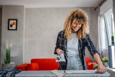 Beyaz, yetişkin bir kadın ev işi ev işi ev işleri ev işleri konsepti için elektrikli ütü kullanıyor.