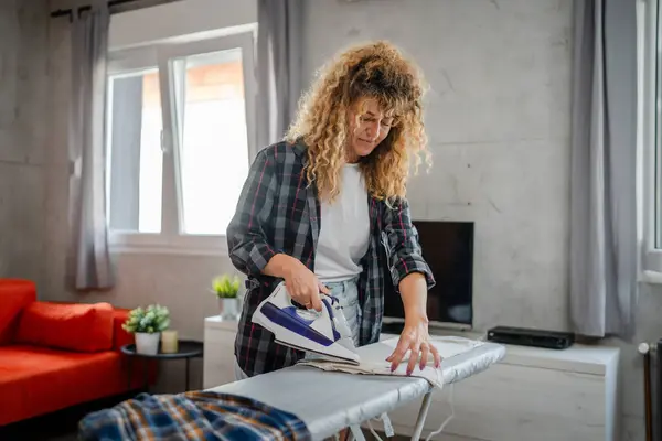 Caucasian adult woman happy female using electric iron for ironing clothes at home housework household chores concept real people domestic work copy space