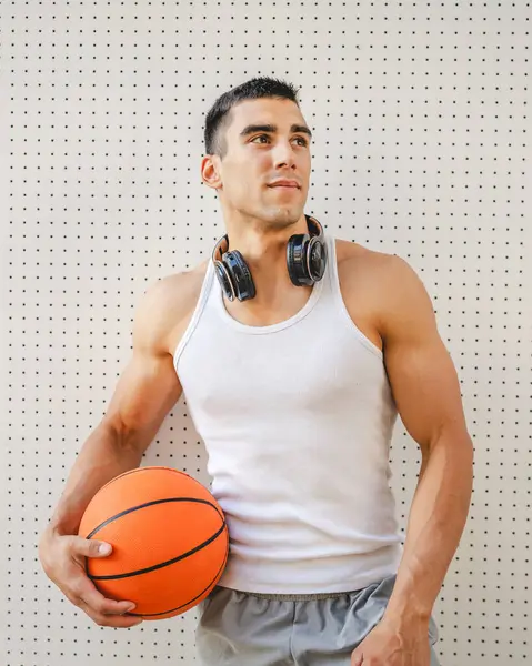 一位年轻的高加索男子运动员站在室外 手握篮球 头戴白色水罐 头戴一件衬衫 肌肉发达 实力雄厚 模仿空间快乐 微笑自信健康的生活方式理念 — 图库照片