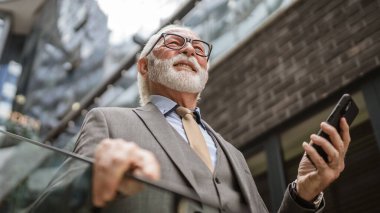 Üst düzey bir işadamı modern binanın dışında duruyor. Telefon etmek ya da mesaj atmak için cep telefonu akıllı telefonu kullanıyor. Gerçek insanlara mesaj atıyor.