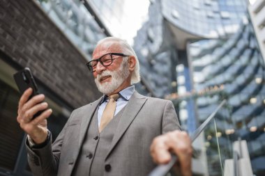 Üst düzey bir işadamı modern binanın dışında duruyor. Telefon etmek ya da mesaj atmak için cep telefonu akıllı telefonu kullanıyor. Gerçek insanlara mesaj atıyor.
