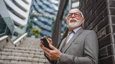 Üst düzey bir işadamı modern binanın dışında duruyor. Telefon etmek ya da mesaj atmak için cep telefonu akıllı telefonu kullanıyor. Gerçek insanlara mesaj atıyor.