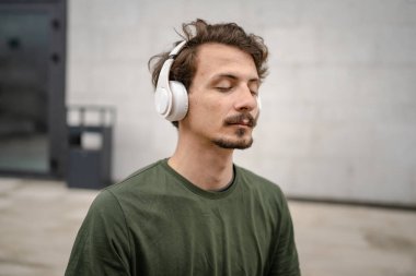 Genç, yetişkin, beyaz bir erkek, yoga ya da meditasyon için kapalı. Kulaklıkla dışarıda otururken iç huzuru ve denge kavramını gerçek insanlara uyguluyor.