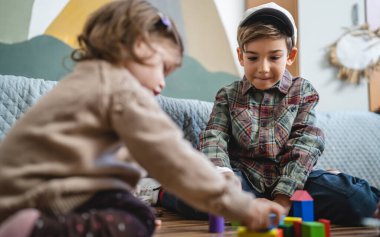 Small caucasian boy and girl siblings brother and sister children play at home sit on the floor at home childhood development growing up concept copy space domestic life