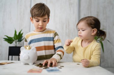 Siblings boy and girl small caucasian child brother and sister play at home with piggy bank saving money childhood investment insurance and finance concept copy space