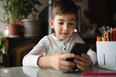 Kafkasyalı bir çocuk anaokulu öğrencisi akıllı cep telefonunu evde tutuyor video oyunları oynuyor ve büyüyen teknoloji bağımlılığı kavramı online tarama için akıllı telefon uygulaması kullanıyor ya da video izlemek için