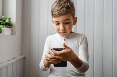 Kafkasyalı bir çocuk anaokulu öğrencisi akıllı cep telefonunu evde tutuyor video oyunları oynuyor ve büyüyen teknoloji bağımlılığı kavramı online tarama için akıllı telefon uygulaması kullanıyor ya da video izlemek için
