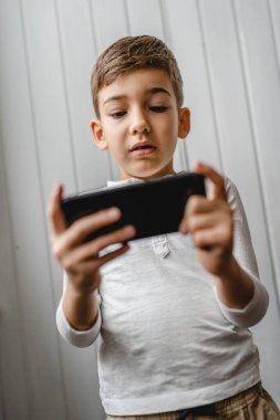 Kafkasyalı bir çocuk anaokulu öğrencisi akıllı cep telefonunu evde tutuyor video oyunları oynuyor ve büyüyen teknoloji bağımlılığı kavramı online tarama için akıllı telefon uygulaması kullanıyor ya da video izlemek için