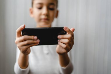 Kafkasyalı bir çocuk anaokulu öğrencisi akıllı cep telefonunu evde tutuyor video oyunları oynuyor ve büyüyen teknoloji bağımlılığı kavramı online tarama için akıllı telefon uygulaması kullanıyor ya da video izlemek için