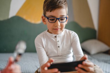 Kafkasyalı bir çocuk anaokulu öğrencisi akıllı cep telefonunu evde tutuyor video oyunları oynuyor ve büyüyen teknoloji bağımlılığı kavramı online tarama için akıllı telefon uygulaması kullanıyor ya da video izlemek için