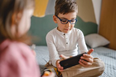 Kafkasyalı bir çocuk anaokulu öğrencisi akıllı cep telefonunu evde tutuyor video oyunları oynuyor ve büyüyen teknoloji bağımlılığı kavramı online tarama için akıllı telefon uygulaması kullanıyor ya da video izlemek için