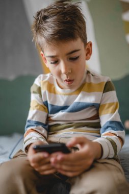 Kafkasyalı bir çocuk anaokulu öğrencisi akıllı cep telefonunu evde tutuyor video oyunları oynuyor ve büyüyen teknoloji bağımlılığı kavramı online tarama için akıllı telefon uygulaması kullanıyor ya da video izlemek için