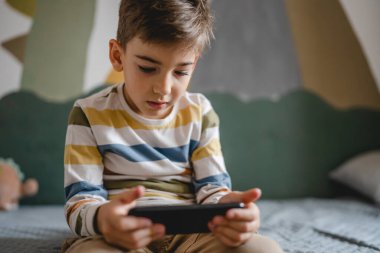 Kafkasyalı bir çocuk anaokulu öğrencisi akıllı cep telefonunu evde tutuyor video oyunları oynuyor ve büyüyen teknoloji bağımlılığı kavramı online tarama için akıllı telefon uygulaması kullanıyor ya da video izlemek için