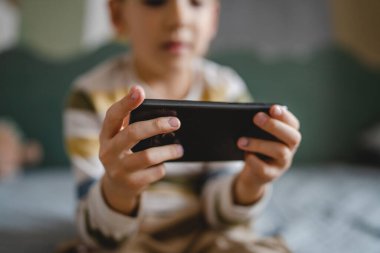 one boy caucasian child preschooler hold smartphone mobile phone at home play video games childhood and growing up technology addiction concept use smartphone app for online browsing or watch video