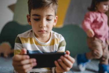 Kafkasyalı bir çocuk anaokulu öğrencisi akıllı cep telefonunu evde tutuyor video oyunları oynuyor ve büyüyen teknoloji bağımlılığı kavramı online tarama için akıllı telefon uygulaması kullanıyor ya da video izlemek için