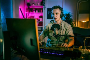 Young man play video games on pc computer while streaming to social media or internet online playtrough or walktrough video male gamer having fun at home wear headphone copy space