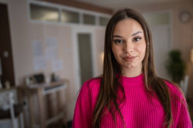 Front view portrait of one caucasian woman young female stand in her apartment at home wear sweater happy confident real people copy space
