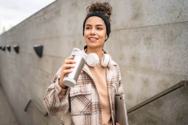 Genç bir kadın yetişkin kız öğrenci ayakta duruyor ya da dışarıda yürüyor dizüstü bilgisayar ve bir fincan kahve tutuyor gerçek bir insan uzayı kopyalıyor mutlu bir gülümseme kulaklıkla gün içinde kendine güveniyor.