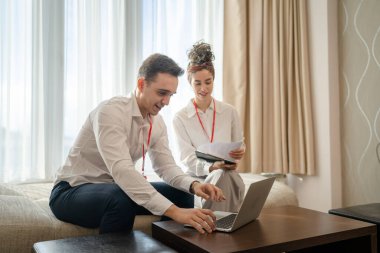 two people man and woman colleagues sitting together at hotel room with contracts and documents preparing for sales meeting or conference making plans sharing experience real people business concept