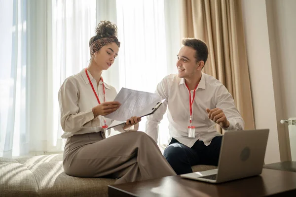 two people man and woman colleagues sitting together at hotel room with contracts and documents preparing for sales meeting or conference making plans sharing experience real people business concept