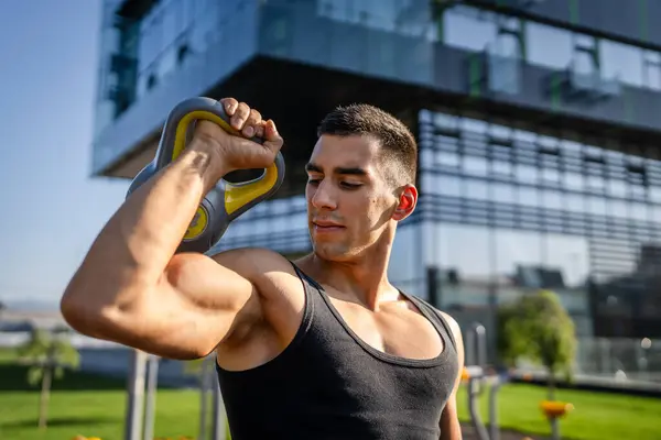 一位年轻的高加索男子肌肉运动员站在室外 用俄罗斯铃铛体重增加体重增加力量 调节耐力 真正的人复制空间 — 图库照片