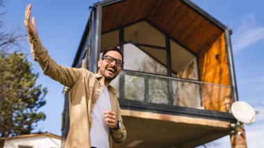 Kafkasyalı yetişkin bir erkek modern küçük ev sahibinin ya da pazarlamacının önünde duruyor. El hareketleriyle davetkar bir gülümsemeye davet ediliyor. Güneşli bir günde mutlu bir gülümseme.