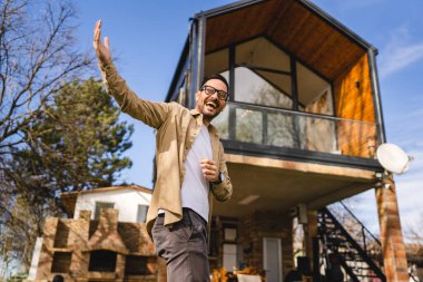 Kafkasyalı yetişkin bir erkek modern küçük ev sahibinin ya da pazarlamacının önünde duruyor. El hareketleriyle davetkar bir gülümsemeye davet ediliyor. Güneşli bir günde mutlu bir gülümseme.