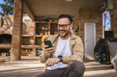 Beyaz tenli, sakallı ve gözlüklü bir adam güneşli bir günde açık havada oturur. Tişört giyer, cep telefonu kullanır. SMS mesajları atar, internete girer, internetten arama yapar.