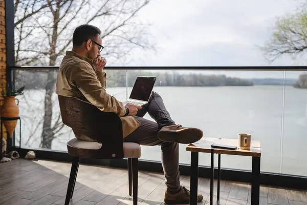 one man adult male 40 years old sit on a terrace balcony with a cup of coffee use laptop computer entrepreneur or freelancer on vacation morning routine real person copy space