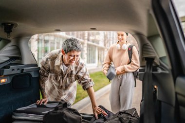 İki güzel bayan öğrenci anne ve kız seyahat kavramı, üniversite kampüsünde yurda taşınırken ya da seyahat ederken bagajları ve diğer eşyaları arabanın arkasından alır.