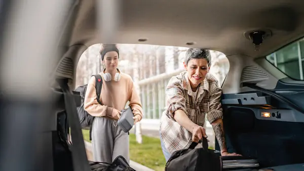 two beautiful women student mother and daughter female travel concept take luggage baggage suitcase and other stuff belongings from back of car while moving into dormitory on college campus or travel