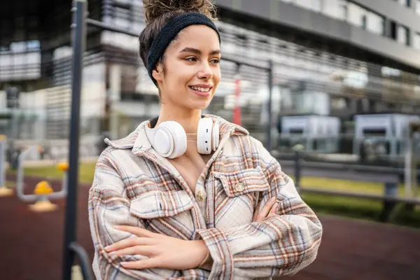One woman young adult generation z caucasian modern female with headphones happy smile stand in the city real person copy space in autumn or spring day