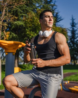 Beyaz tenli genç bir erkek sporcu açık hava spor salonunda çalışırken fren yapıyor. Elinde destek malzemesi tutuyor. Kendine güveni tam, güçlü, güçlü bir kopya alanı var.